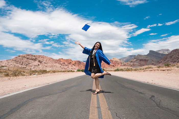 Senior high-school graduate celebrating in the middle of a desert road