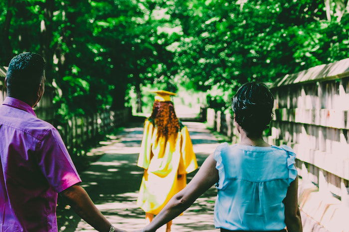 senior picture idea of a senior high-school graduate walking with her parents behind her