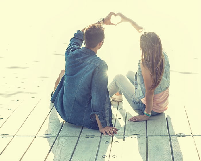 Couple making a heart with their hands against the setting sun, sitting on a dock