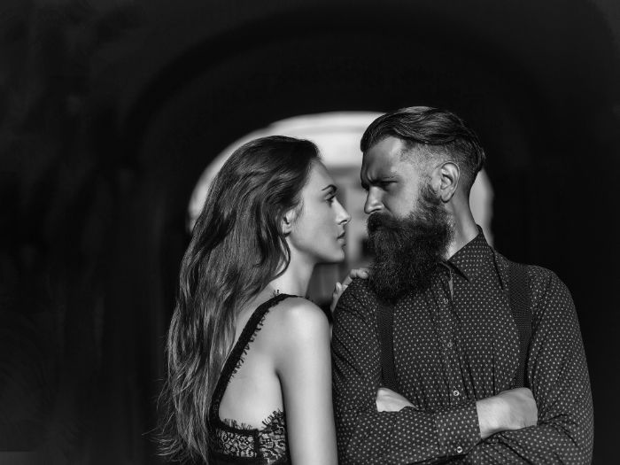 Striking black and white photo of a coiple under a bridge, staring intently at each other