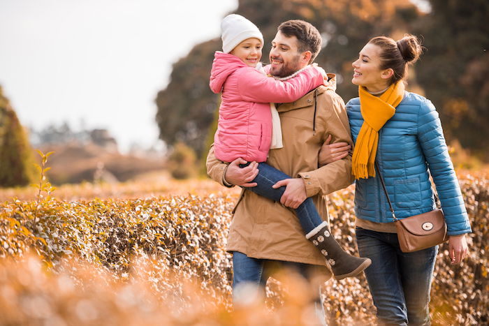 A family of three outdoors in a park with a man holding a child