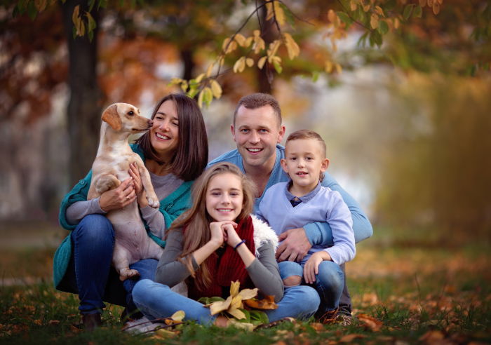 A family sitting in a fall forest with a woman holding a dog