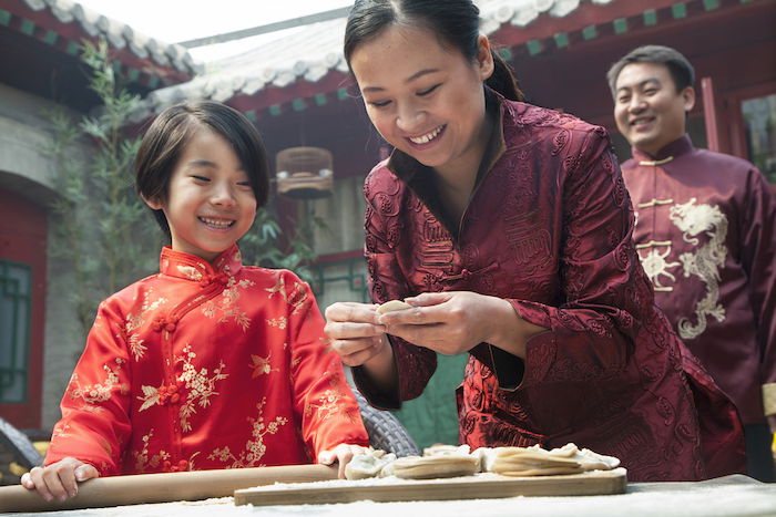 A mother and daughter preparing food with the father looking on in the background