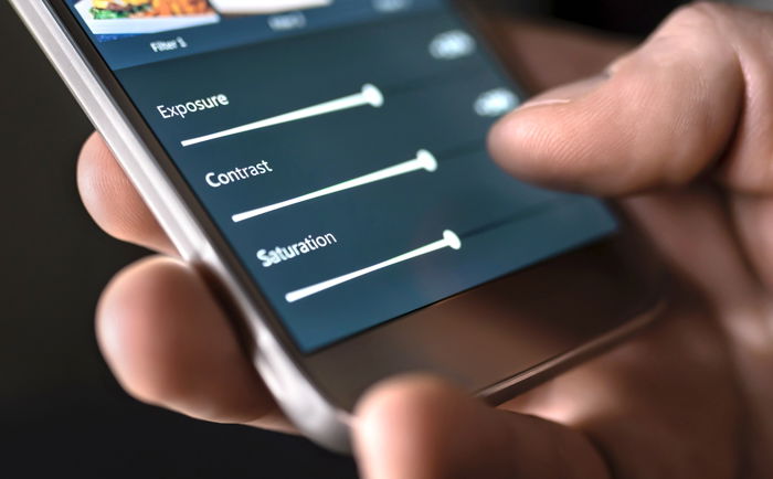 A photographer edits the exposure, contrast, and saturation of an image on his smartphone