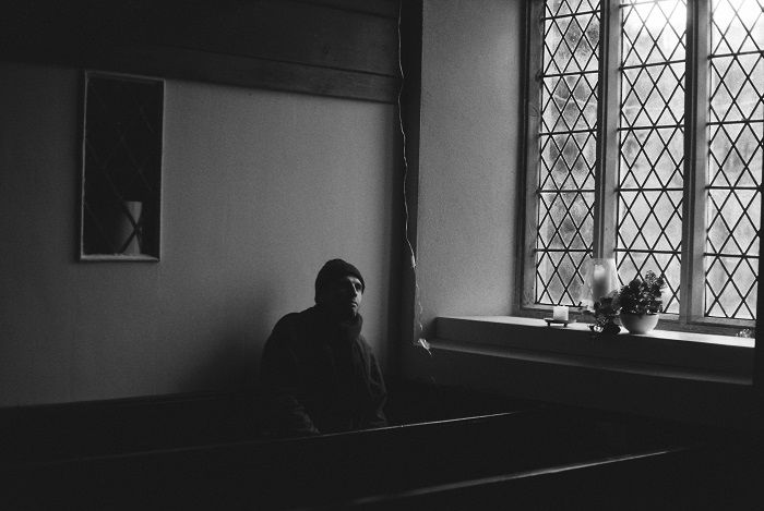 Black and white image of young man sitting in a church next to the window