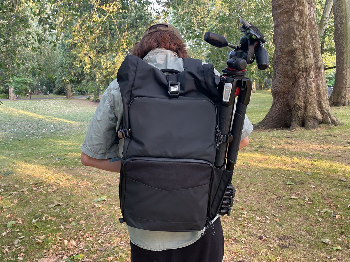 Back view of the Tenba DNA camera backpack being worn with a tripod attached to its side