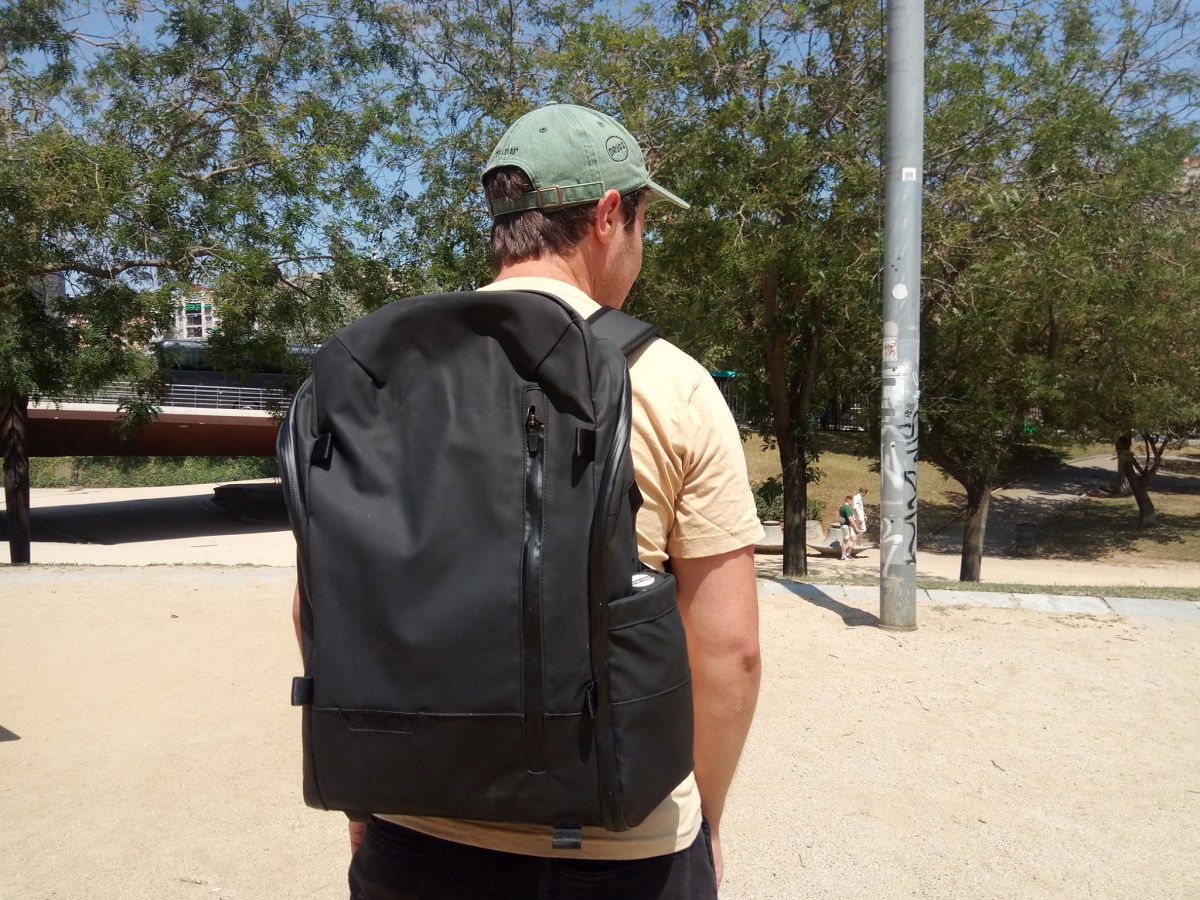 A person standing on a sidewalk, wearing a backpack.