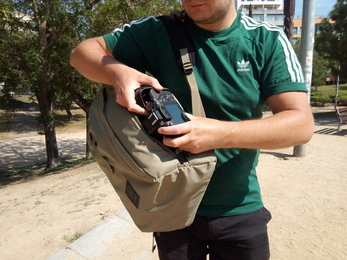 A man in the middle of setting up his camera, which is attached to a backpack. 