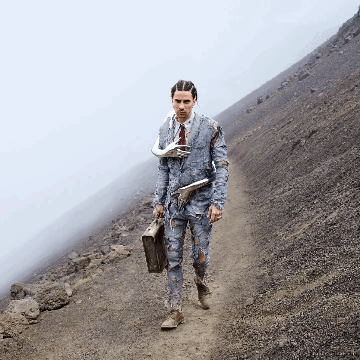 A business man in a tattered suit walking with chrome arms around him