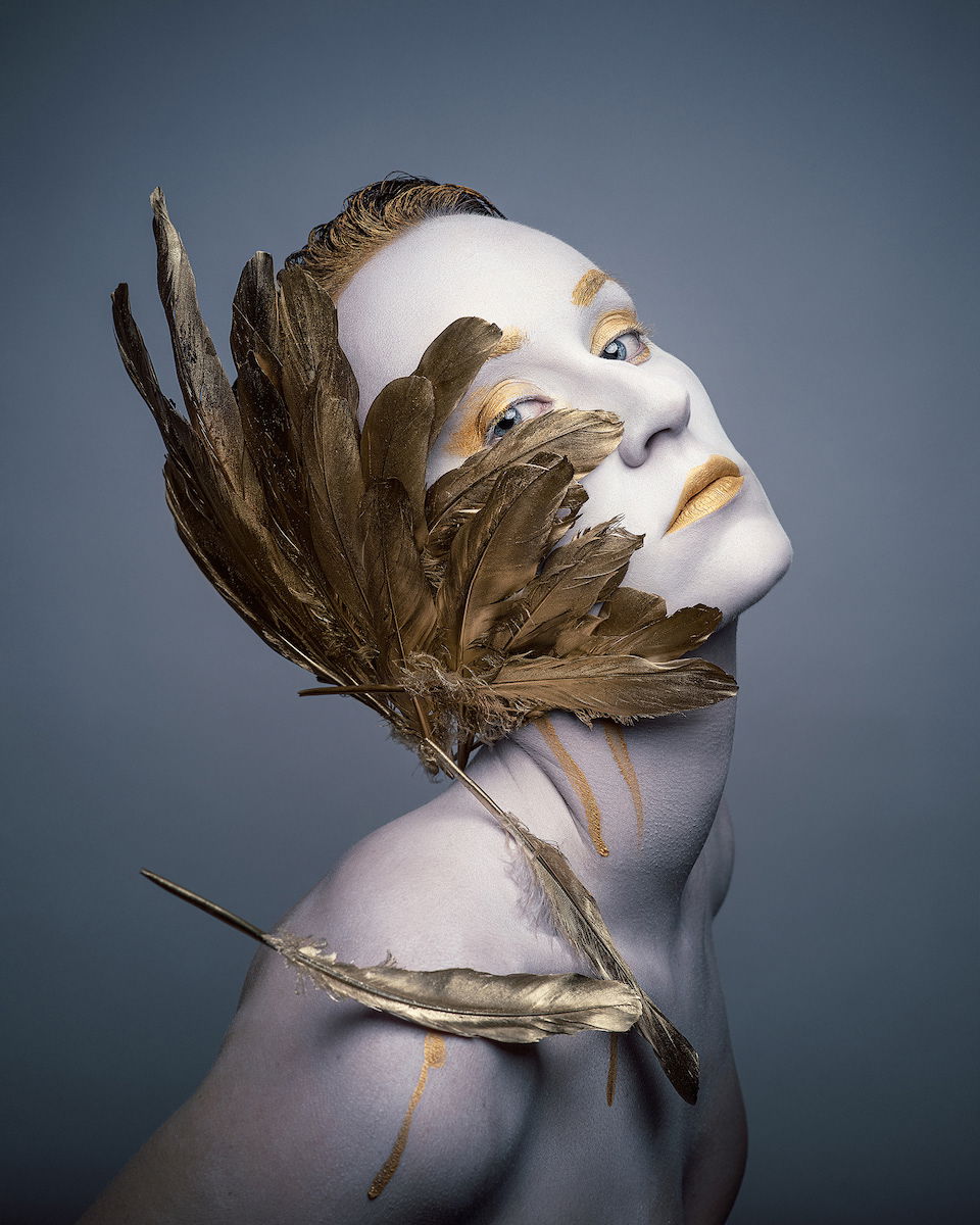 A stylized headshot of a woman with a large gold leaf and makeup