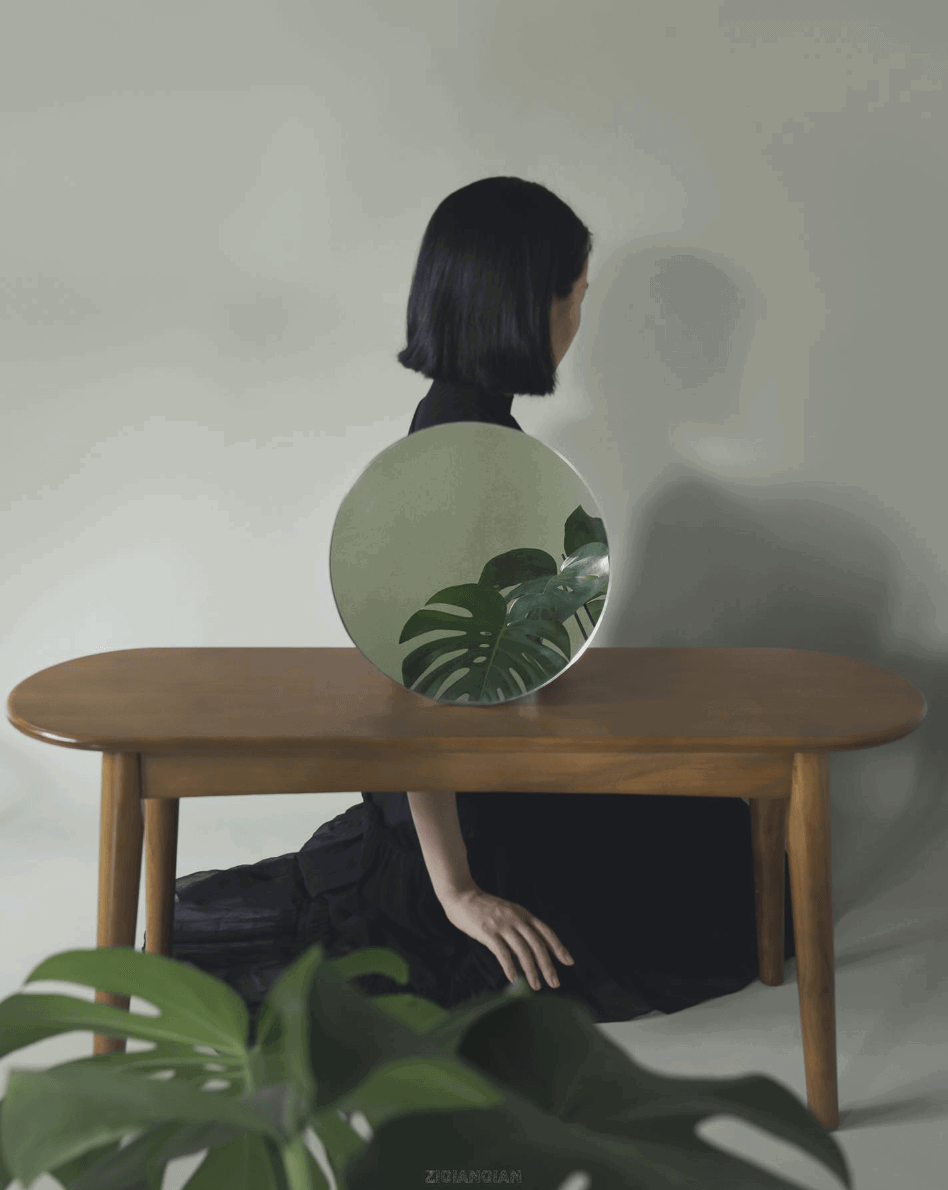 A woman posing with her back turned and a mirrored plant and table