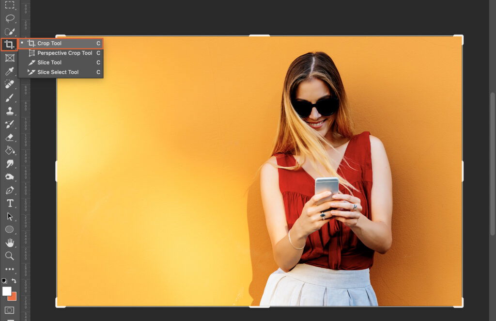  A woman is standing in front of a yellow background, looking at her phone. 