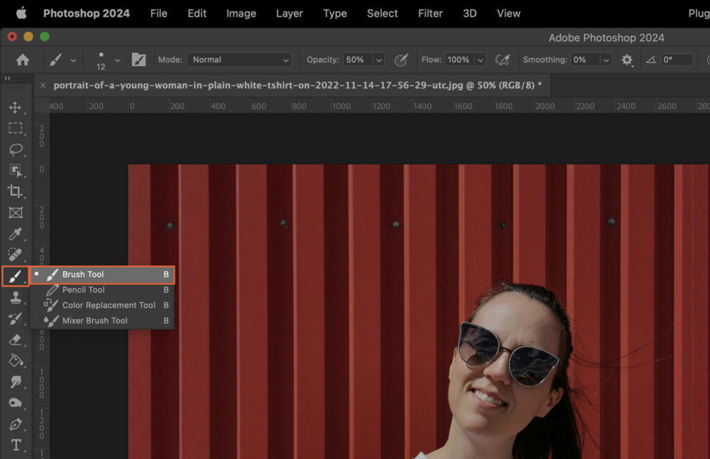 A woman standing in front of a red wall with a building pattern behind her, smiling at the camera.