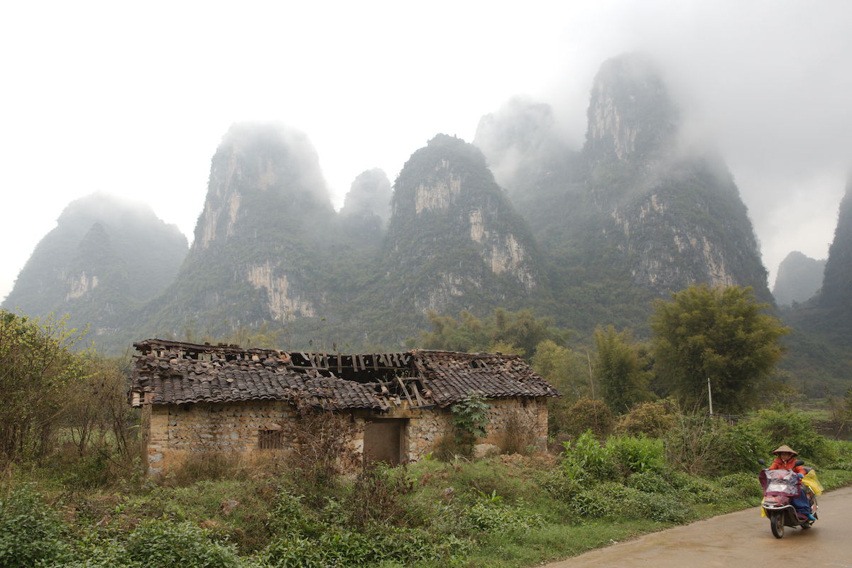 Original unedited photo of motorcyclist in a rural area with building and karsts