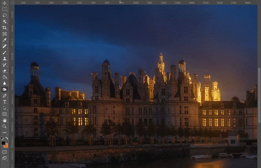 A dark sky over a castle, with the city lights glowing in the background. 