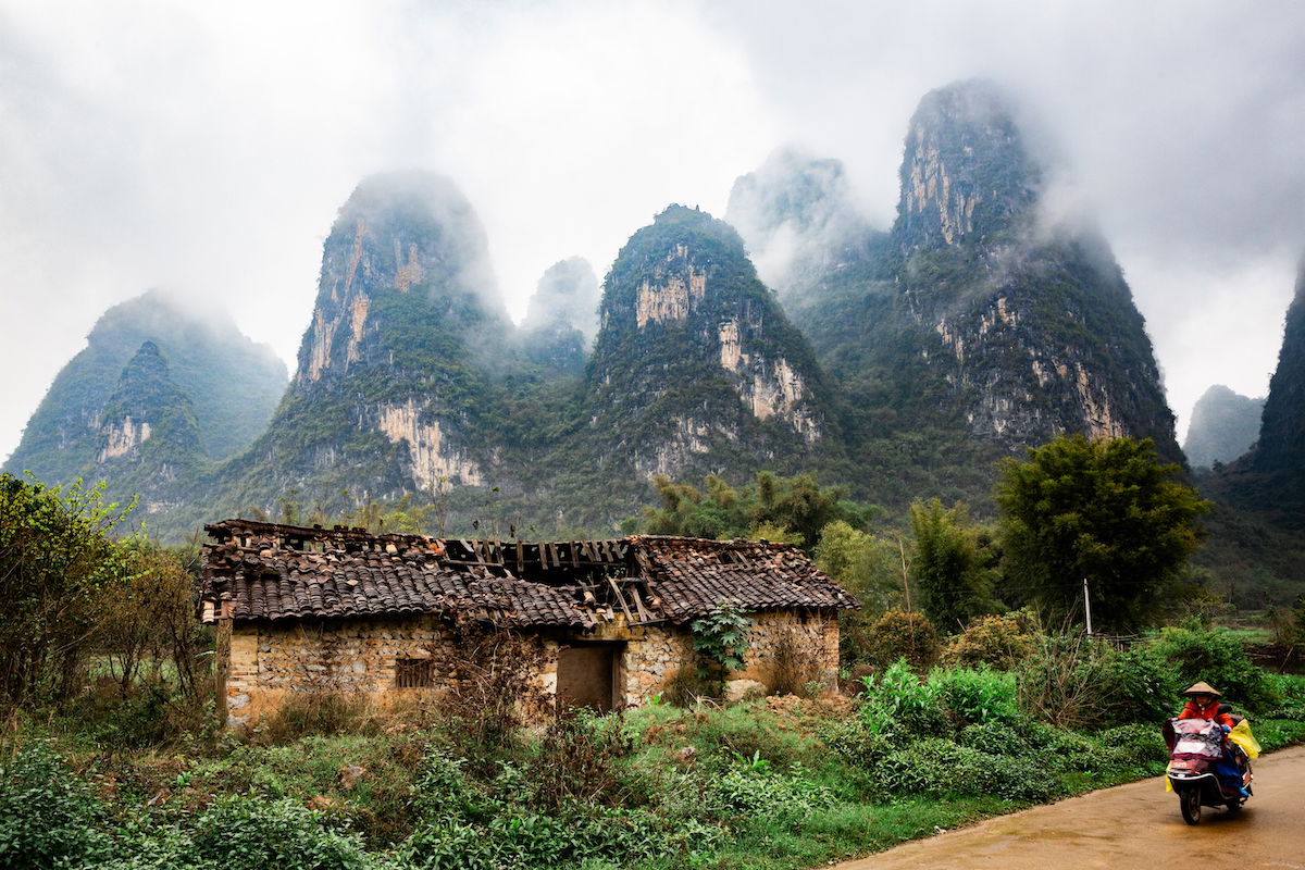 Original image of a motorcyclist riding through landscape with a building and karsts