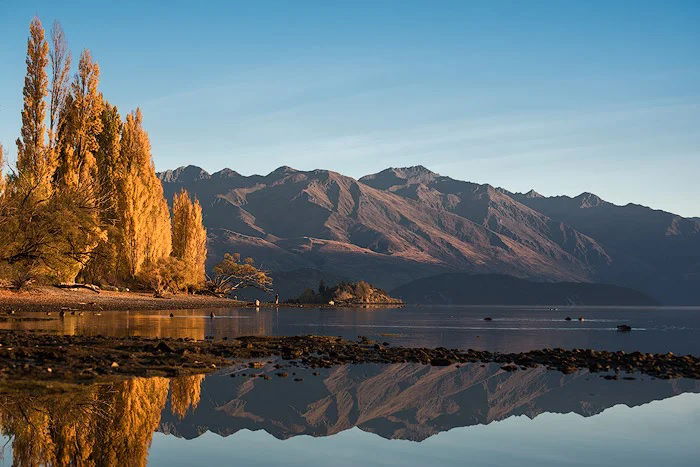 Landscape with lake in the foreground, trees on the left side, and mountains in the background