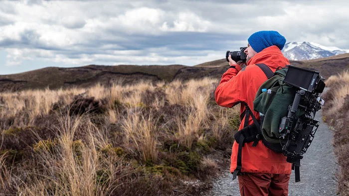 Photographer taking a photo outdoors with a full hiking pack