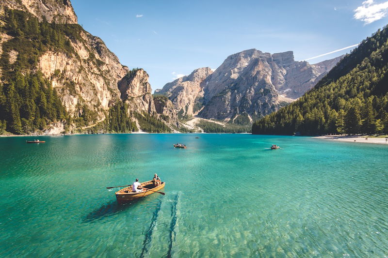 a landscape image of a lake with a people in a small boat in the foreground and mountains in the background with a deep depth of field