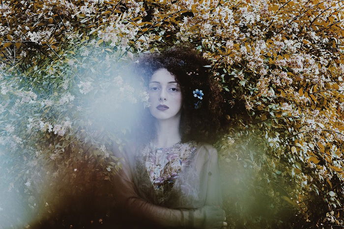 Woman with curly hair in front of a large flowery shrub 