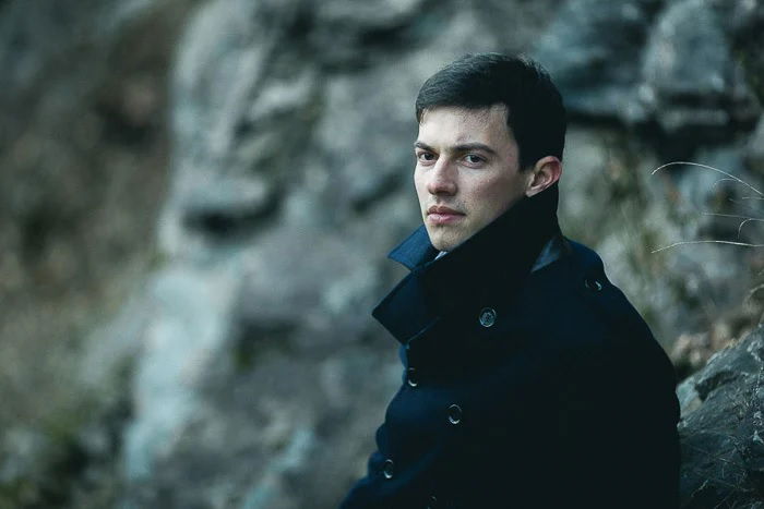 Portrait of man in big coat leaning on some big rocks