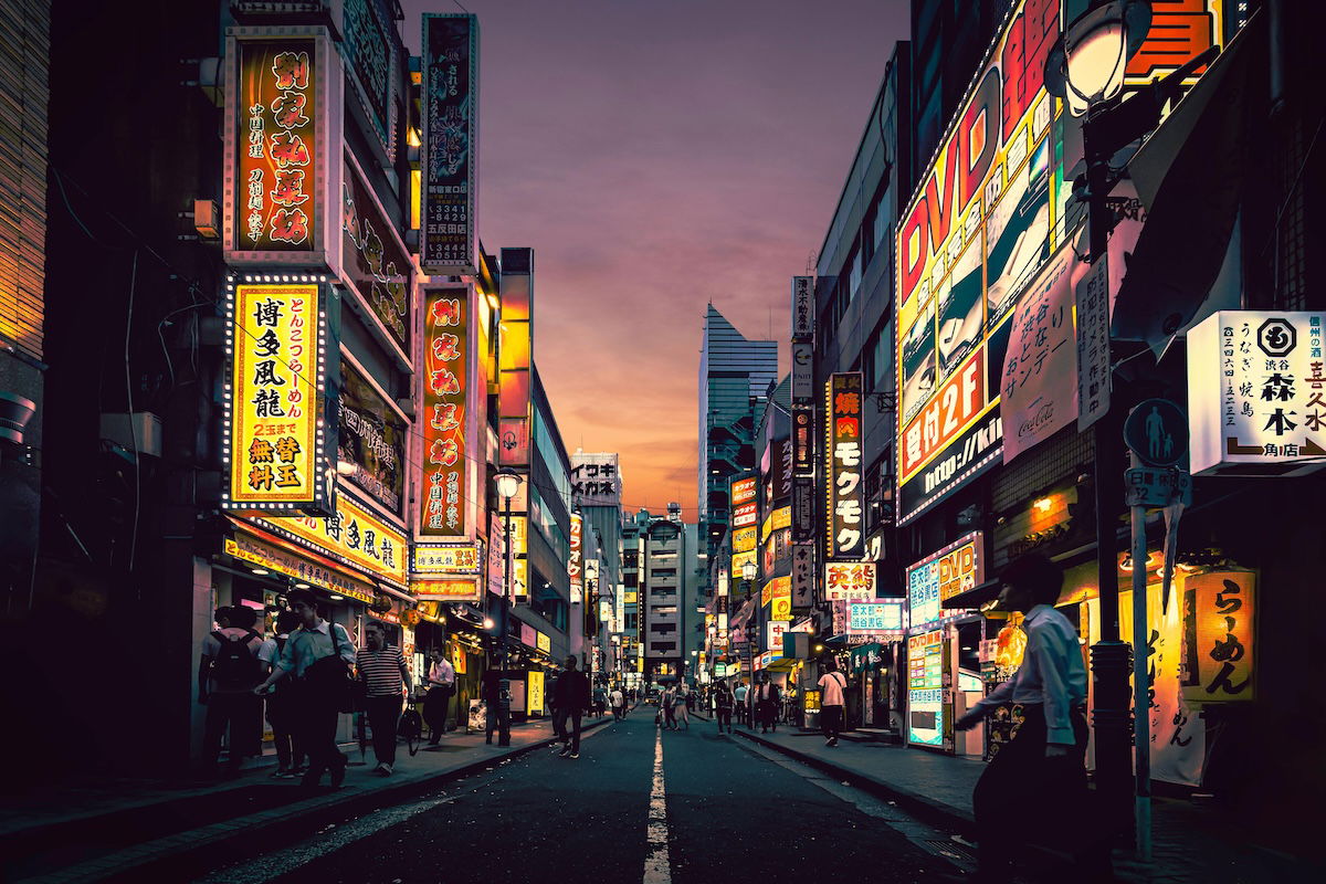 A bustling street at dusk with neon signs and illuminated buildings, showcasing the vibrancy of urban life. 