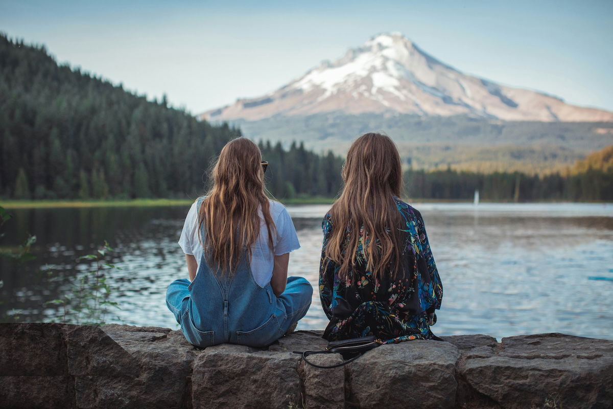 Two people sit on a wall with a stunning mountain in the background.