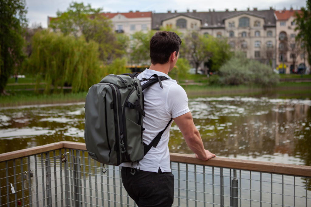 A man with a backpack looking over a fence by a pond.