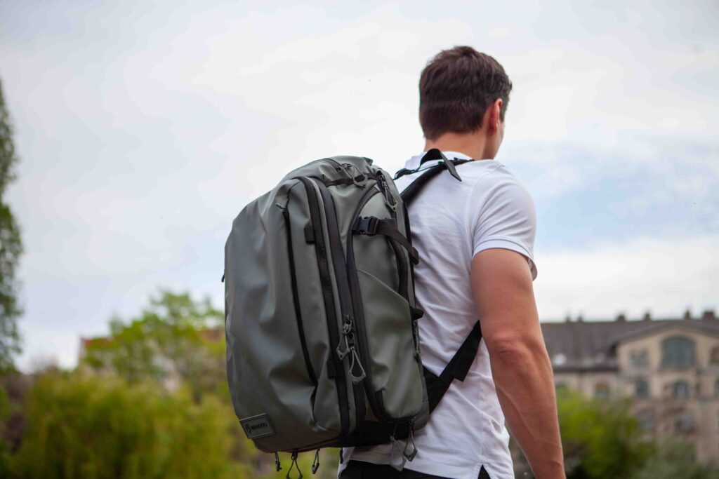 A man in a white shirt and green backpack is standing on the grass with his back to the camera.