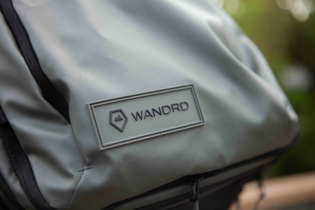 A grey and black backpack with a name tag attached, sitting on a wooden bench. 