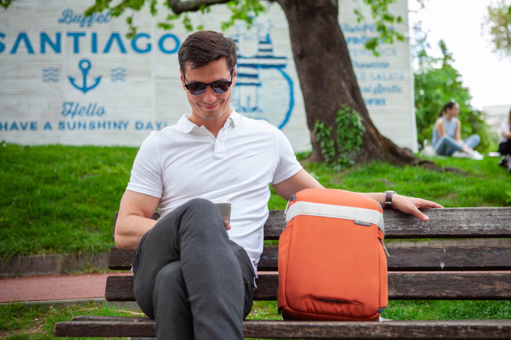 Man sitting on a bench with a Nomatic Luma Camera Pack next to him