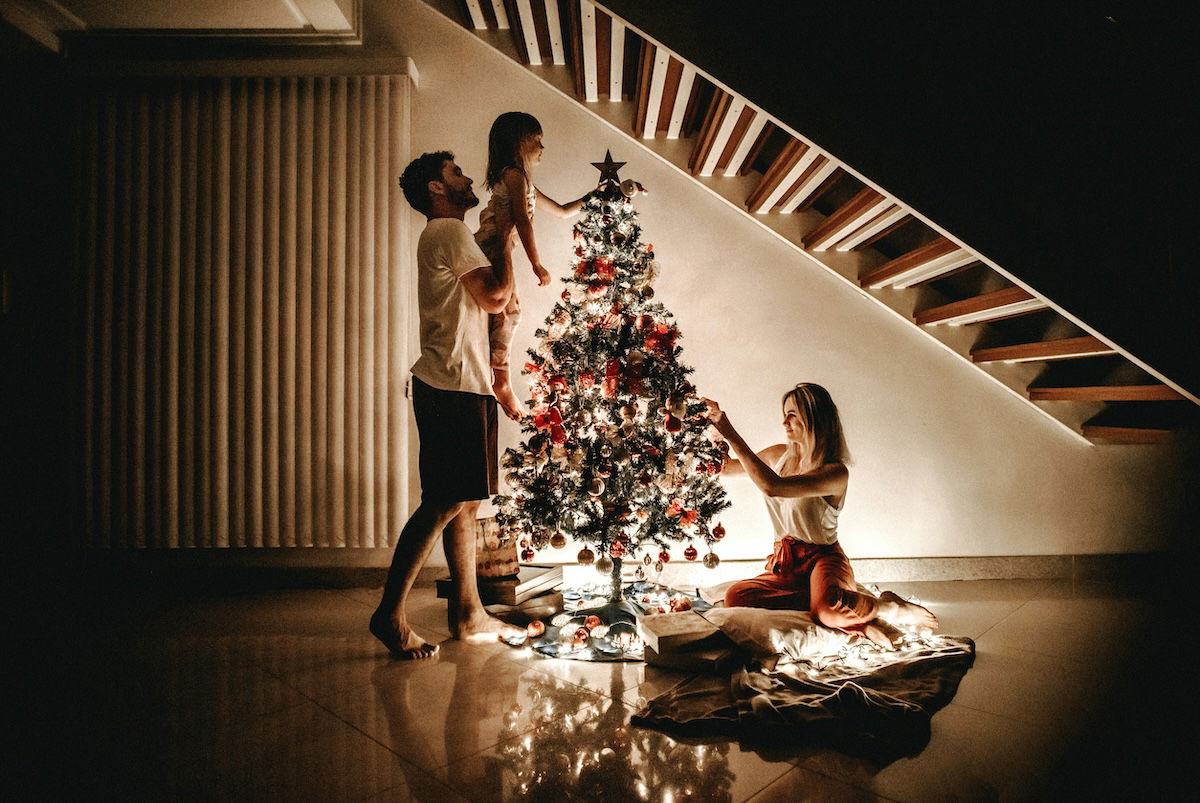 A family of three is gathered around a Christmas tree, decorated in a festive manner. 