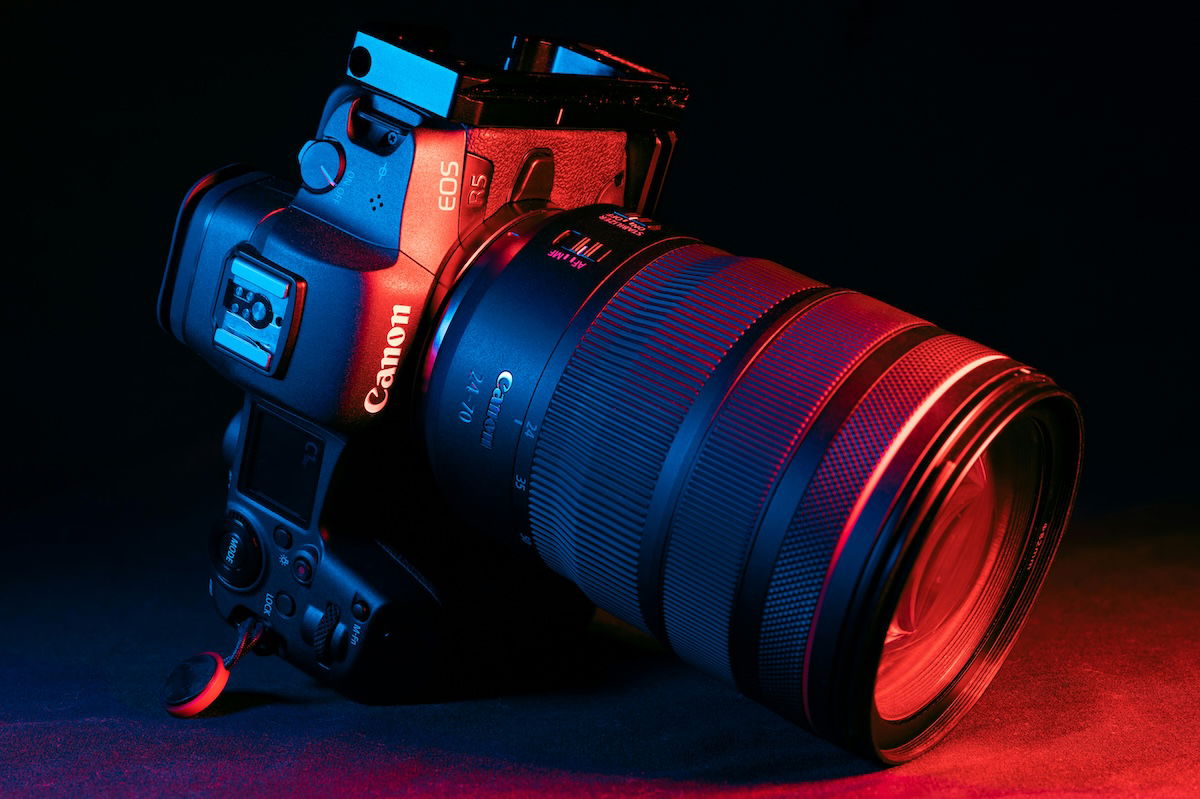 A Canon DSLR camera with a red lens and a black strap, set up on a tripod. 