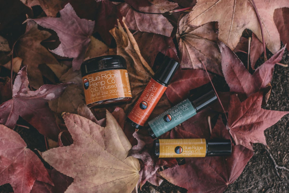 A collection of bottles containing various oils and balms, arranged on a leaf-strewn surface with the theme of fall. 