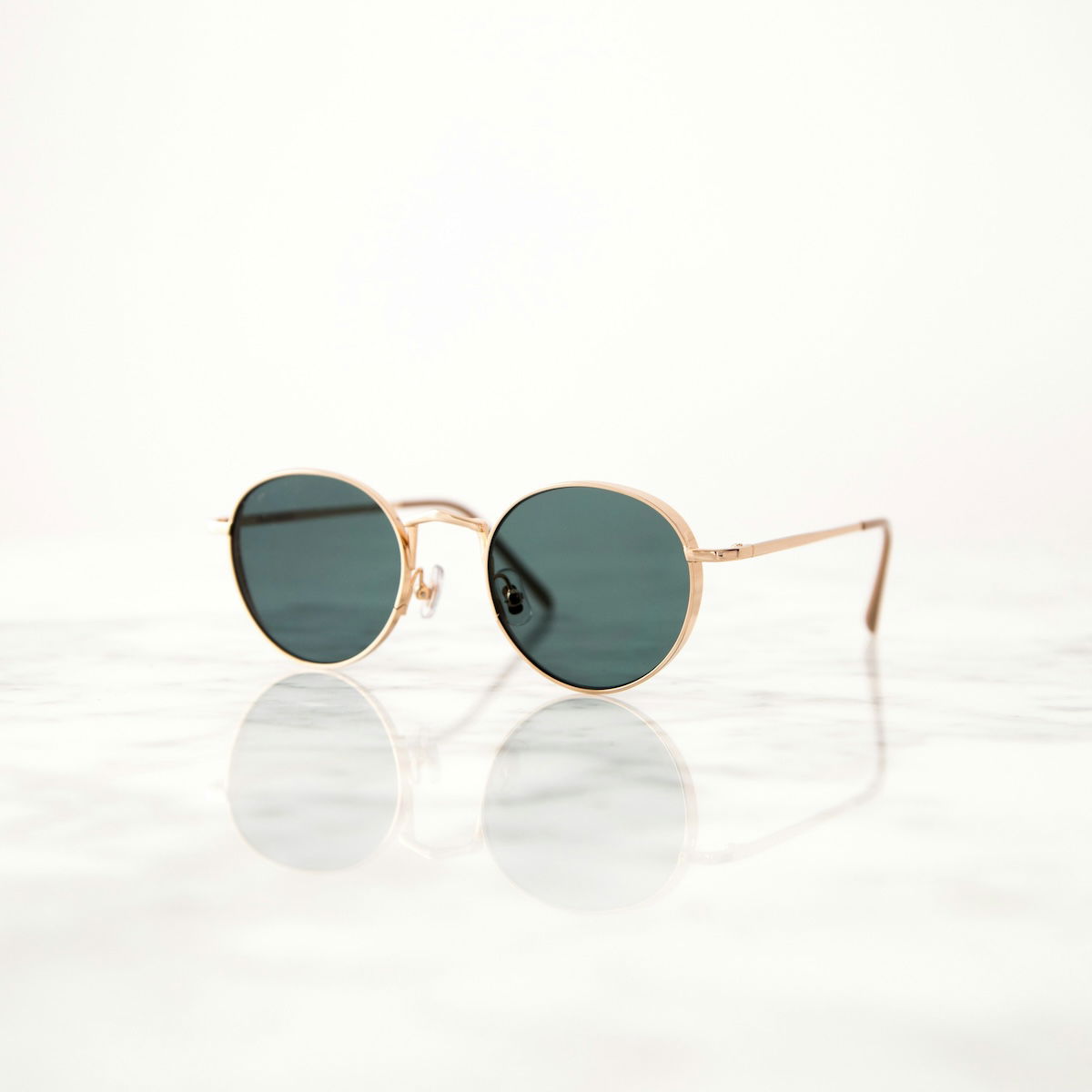 A pair of rose gold sunglasses with dark blue lenses resting on a reflective surface, possibly a marble table. 