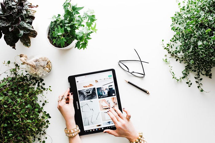 Woman's hands holding an iPad surrounded by potted plants.