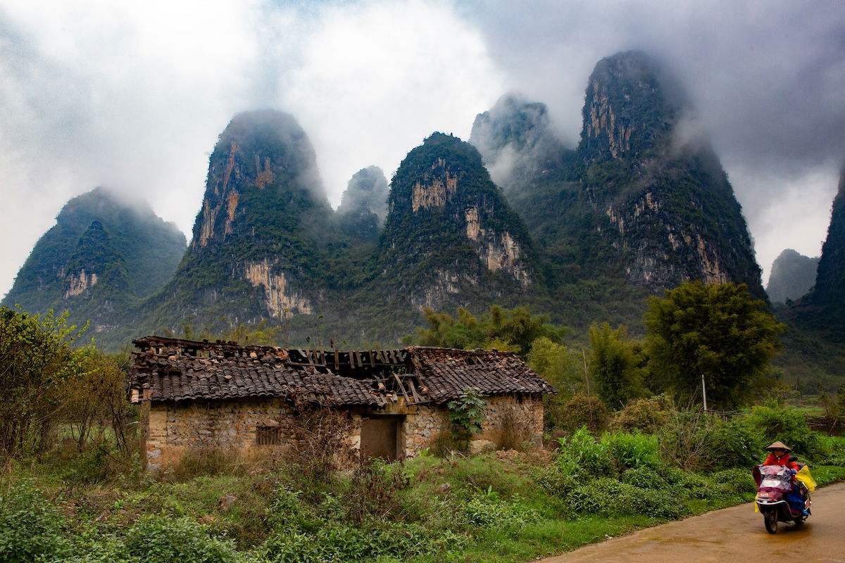 Photograph of mountains in the mist with a abandoned shed in foreground and person on a moped with full dehaze