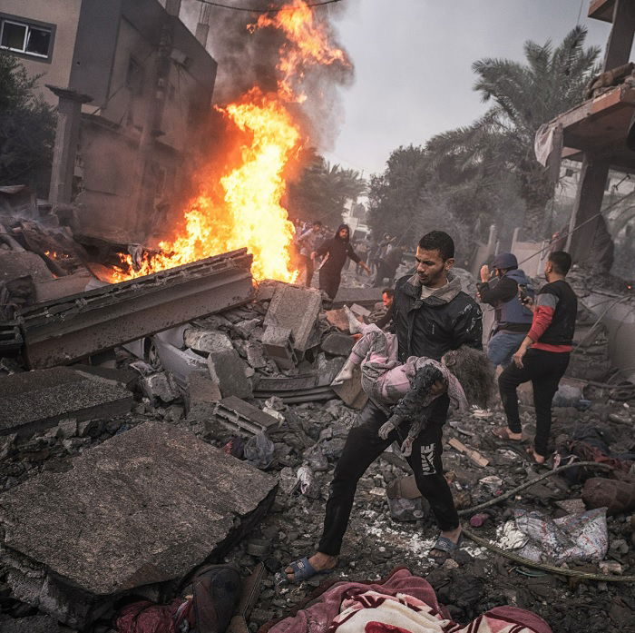 Man carrying dead girl through flaming rubble