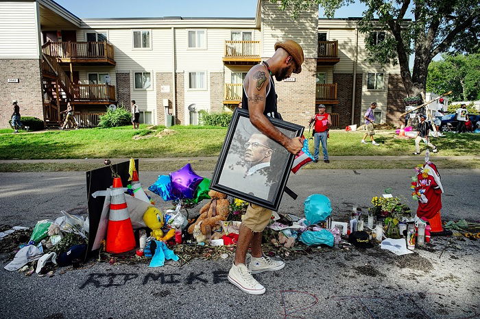 Man holding picture of Malcolm X looking at street memorial