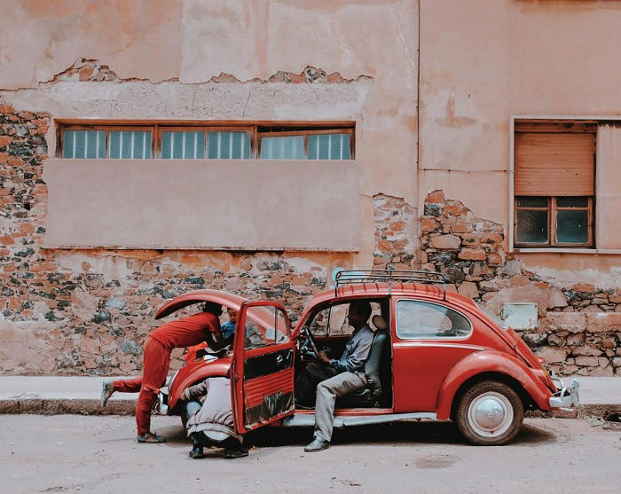 Three men fixing an old red VW beetle