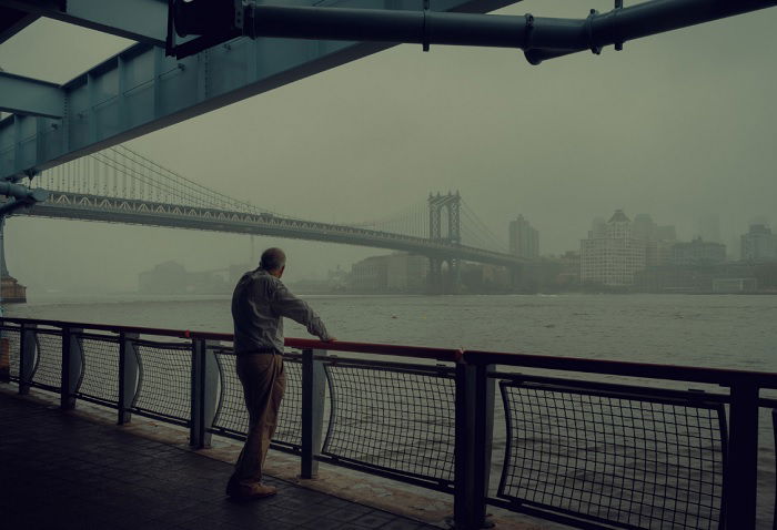 Elderly man looking out onto a city river