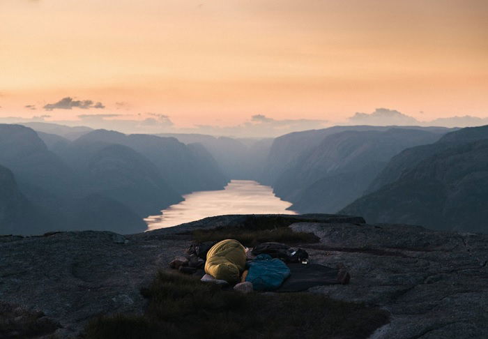 Two sleeping bags on rocky ledge in front of mountain valley