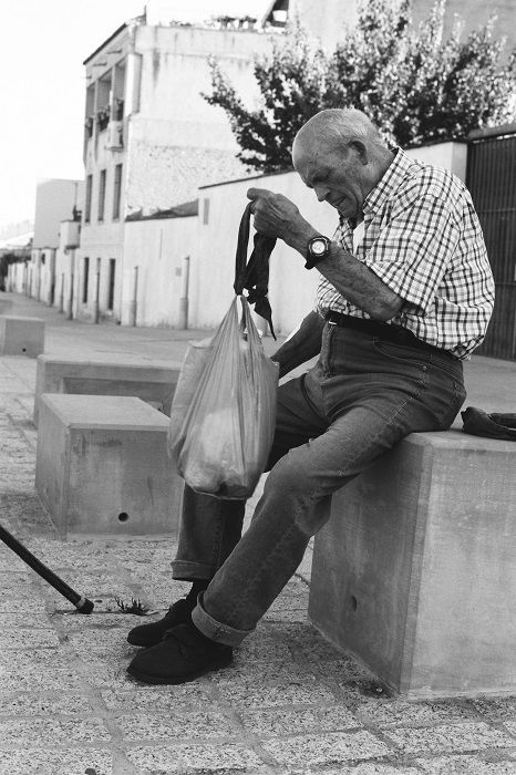 Old man with plastic bag perched on a bench