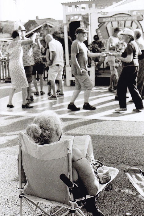 Woman in camping chair reading with dancers in the background