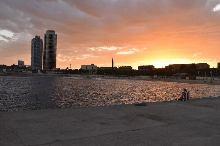 Man sitting on pier by two towers in Barcelona beach